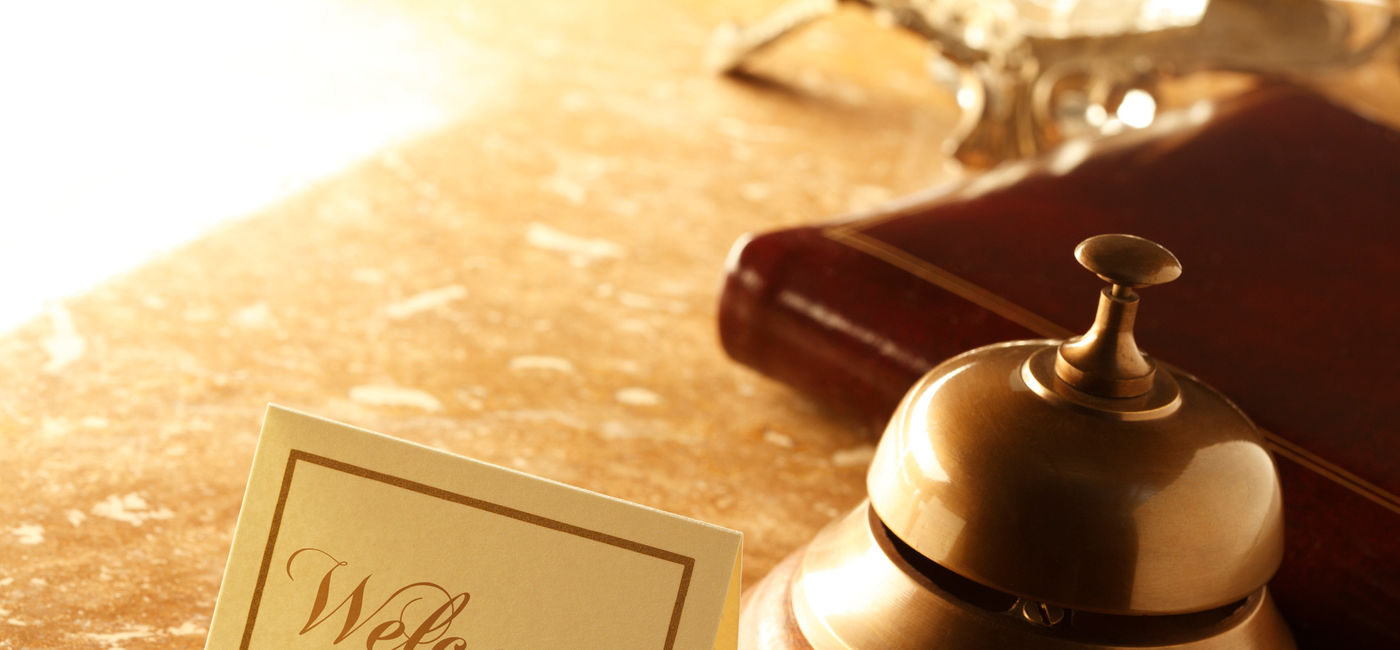 Image: Welcome card and service bell sitting on a hotel reception desk. (photo via iStock/E+/DNY59)